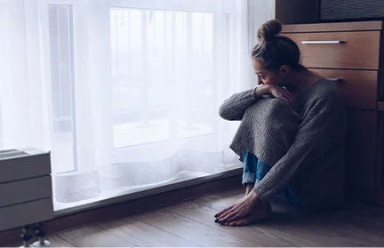 Sad woman sitting on floor near window experiencing extreme sadness because of bipolar disorder