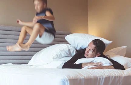 a child jumping on his bed while his dad is watching him. he is experiencing hyperactivity