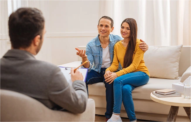 An image capturing a couple seated on a couch, sharing genuine smiles during a couples counseling session. Their engaged and open interaction reflects the positive dynamics of seeking support through couples therapy in Bucks County, PA, to strengthen relationships and foster mutual understanding.