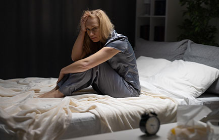 a woman sitting on a bed, whose sleep was disturbed because of anxiety